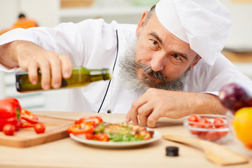 Close up portrait of professional senior chef decorating meat steak with olive oil and vegetables, copy space