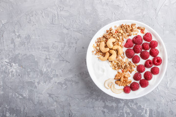 Yoghurt with raspberry, granola, cashew and walnut in white plate  on gray concrete background and linen textile. top view.