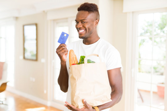 African american man holding paper bag full of groceries and holding credit card as payment