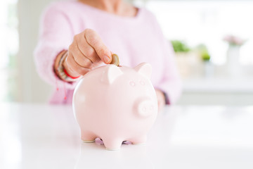 Close up of senior woman putting a coin inside piggy bank as savings