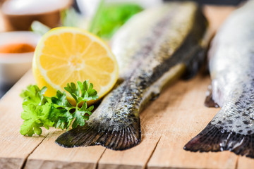 Fresh rainbow trout tails with lemon and green leaves. Fishes on wooden board, selective focus.