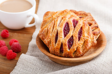 puff pastry buns with strawberry jam on wooden background with linen textile and a cup of coffee. side view.