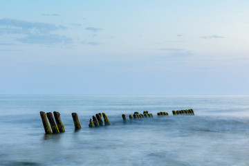 long exposure smooth sea surface with breakwater sticking out of the water in blue twilight