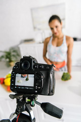 selective focus of digital camera with sportswoman gesturing near vegetables