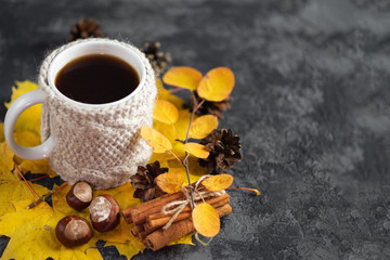 Cozy autumn or winter morning at home. Mug of coffee in a knitted jacket. Autumn colorful leaves on the table and a cozy weekend relaxation