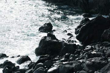 Volcanic stones on ocean shore, cold clean water, waves, Madeira island, Portugal
