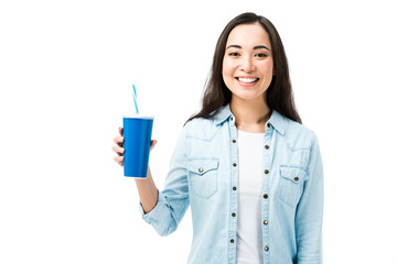 attractive and smiling asian woman in denim shirt holding plastic cup isolated on white