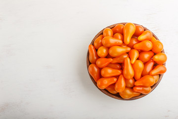 Fresh orange grape tomatoes in wooden bowl on white wooden background. top view.