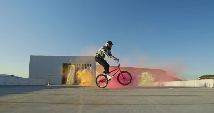 BMX rider on a rooftop jumping and using smoke grenades