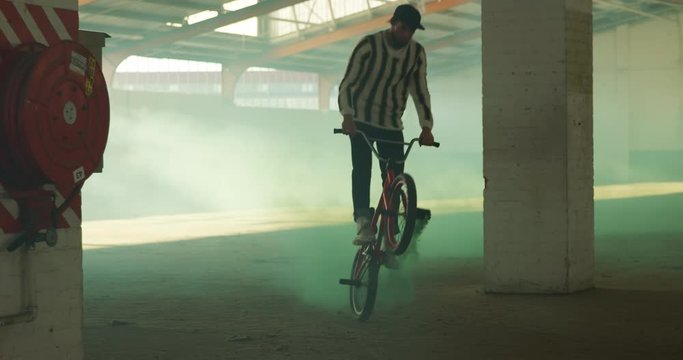 BMX riders in an empty warehouse using smoke grenade