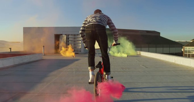 BMX rider on a rooftop jumping and using smoke grenades