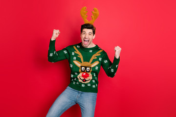 Portrait of funny funky crazy man raise fists scream yeah celebrate christmas time party event wear stylish deer reindeer pattern pullover isolated over red color background