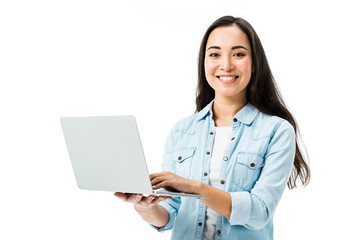 attractive asian woman in denim shirt smiling and holding laptop isolated on white