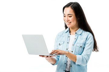 attractive asian woman in denim shirt smiling and holding laptop isolated on white