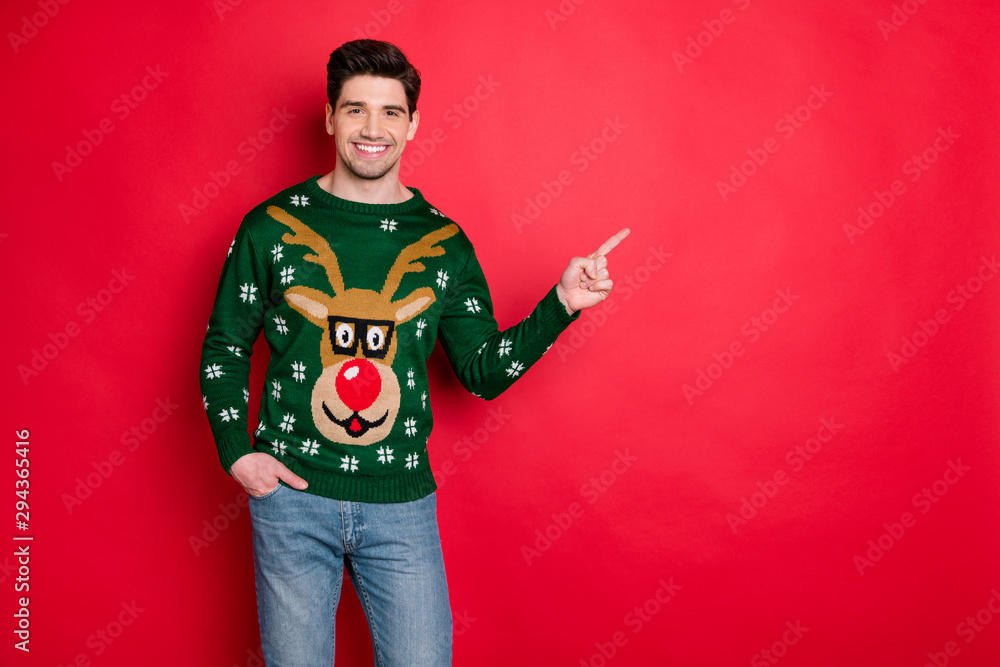 Sticker Portrait of content cheerful funny man in deer reindeer point index finger at copy space recommend shopping christmas ads wear denim jeans isolated over red color background