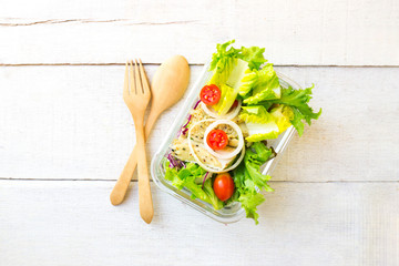 Vegetable salad with chicken on glass box  wooden spoon and fork on white wood table.Top view.