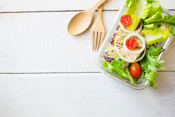 Vegetable salad with chicken on glass box  wooden spoon and fork on white wood table.Top view.