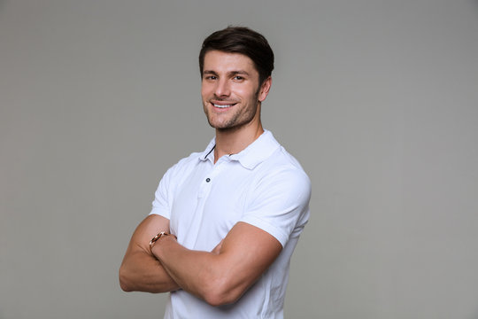 Image of happy brunette man smiling at camera with hands crossed