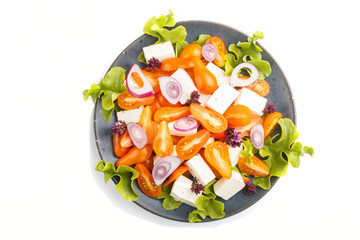 Vegetarian salad with fresh grape tomatoes, feta cheese, lettuce and onion on blue ceramic plate isolated on white background, top view.