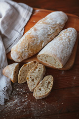 Chiabatta homemade bread. Fresh baked bread on a kitchen board and wooden background. White bread and chopped slices.