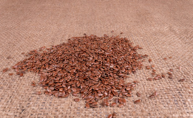 Close-up side view of a small amount of linen brown seeds laying on the sackcloth