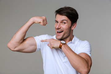 Image of optimistic brunette man smiling and showing his bicep