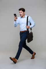 Full length portrait of businessman walking with smartphone and laptop bag