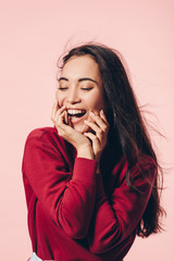 attractive asian woman with closed eyes in red sweater smiling isolated on pink