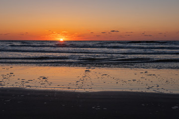 Obraz premium Beautiful sunset landscape at the North sea and orange sky above it with awesome sun golden reflection on waves as a background. Amazing summer sunset view on the beach.