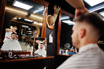 Young bearded man getting haircut by hairdresser while sitting in chair at barbershop. Barber soul.