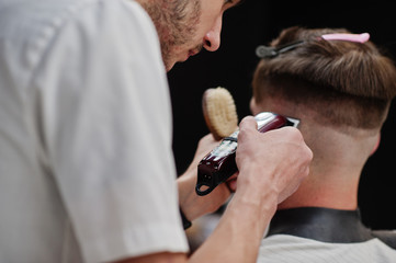 Young bearded man getting haircut by hairdresser while sitting in chair at barbershop. Barber soul.