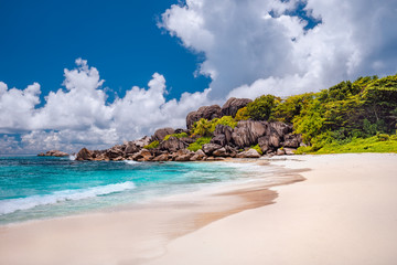 Grand Anse exotic beach at La Digue island in Seychelles. White sandy beach with blue ocean lagoon, white waves and granite rocks in background