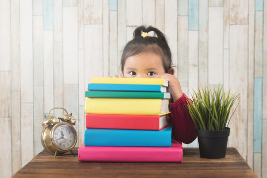 Cute Little Asian Girl Peeping From Behind Stack Of Books. Concept Of Education, Couriousity And Child Growth Development