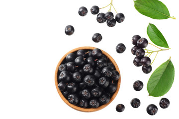Chokeberry in wooden bowl with green leaves isolated on white background. Black aronia. Top view.