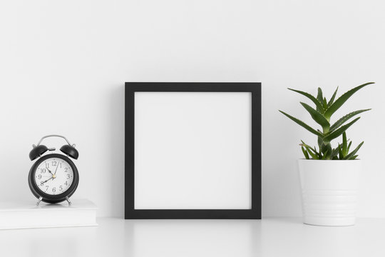 Black square frame mockup with a aloe vera in a pot and workspace accessories on a white table.