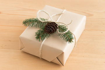 Fototapeta na wymiar Kraft christmas gift with pine cone and leaves on a wooden table.