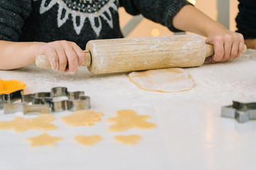 Detail of young kids baking Christmas gingerbread cookies in house kitchen on winter day. Child with rolling pin baking cookies. Baking and cooking with children for Christmas at home.Selective focus