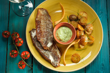 Grilled sea sauce in creamy sauce and pesto with rustic baked potatoes on a blue wooden background with a sprig of cherry tomatoes