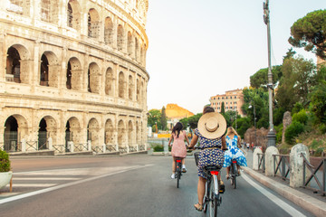 Obraz premium Three happy young women friends tourists with bikes at Colosseum in Rome, Italy at sunrise.