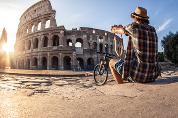 Happy young man tourist wearing shirt and hat with bike taking pictures with vintage camera at...