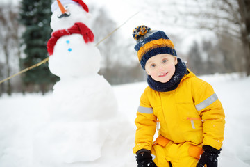 Fototapeta na wymiar Little boy playing with funny snowman. Active outdoors leisure with children in winter.