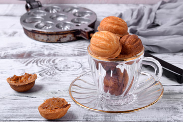 Walnut shaped cookies with caramel in a glass cup on the white table. Special skillet in the background
