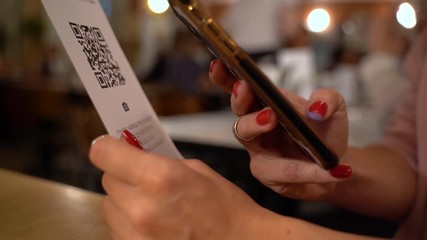 Scanning QR code with smart phone. The woman reads the bar code using the application on the smartphone in cafe