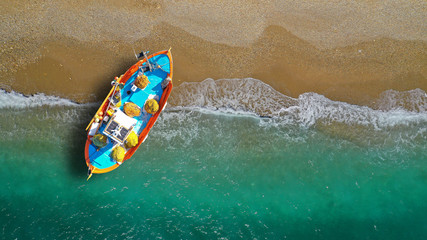 Fototapeta premium Aerial top view photo of red traditional wooden fishing boat in Aegean island destination beach with emerald sea