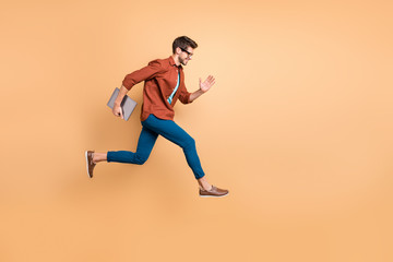 Fototapeta na wymiar Full length body size view of his he nice attractive cheerful cheery successful brunet guy jumping in air carrying laptop running fast late hurry-up isolated over beige color pastel background