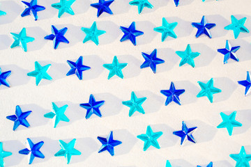 Fototapeta na wymiar Light and dark blue rhinestones in the form of stars lie on a light pearl background. Festive background, party concept. Top view, minimalism, flat lay.
