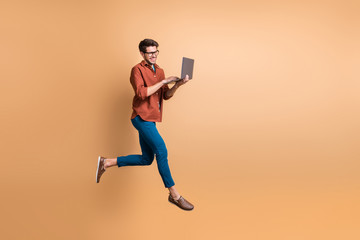 Fototapeta na wymiar Full length body size view of his he nice attractive cheerful cheery glad brunet guy jumping in air using laptop part-time job isolated over beige color pastel background