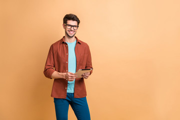 Portrait of his he nice attractive cheerful cheery successful content brunette guy holding in hands digital e-book browsing web app isolated over beige color pastel background