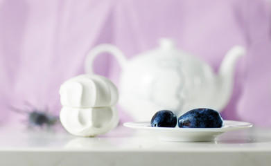 Plums on the white plate and tasty marshmallow on lavender background