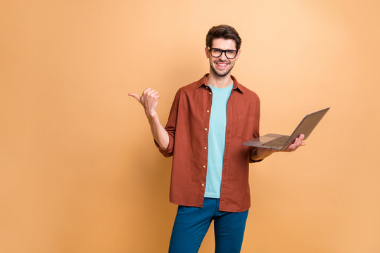 Portrait of his he nice attractive cheerful successful content brunet guy holding in hands laptop pointing thumb aside ad advert solution isolated over beige color pastel background